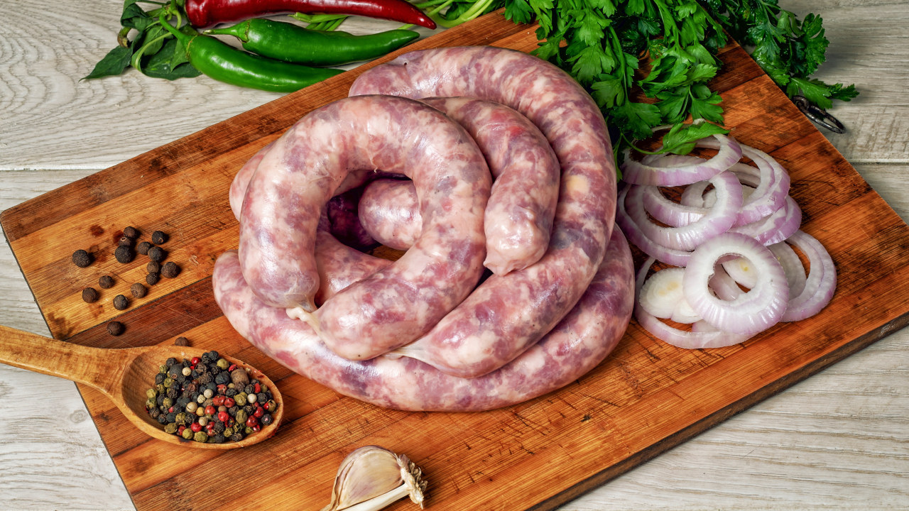 Skärbräda i träö med följande på: stoppade, olagade korvar, skivad rödlök, persilja, hela pepparkorn i träsked, vitlök, chilifrukter.